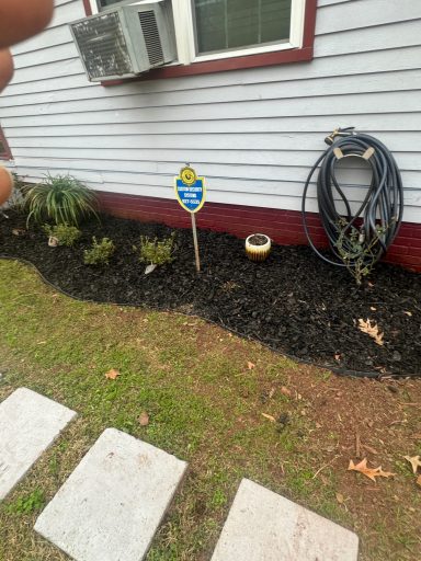 A garden area featuring a sign, mulch, and decorative plants near a house's exterior.